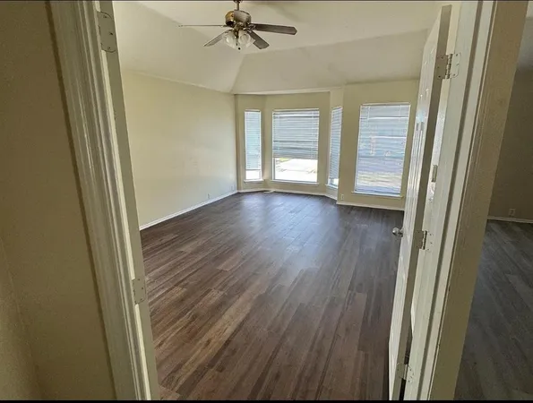 an empty room with wooden floor fan and windows