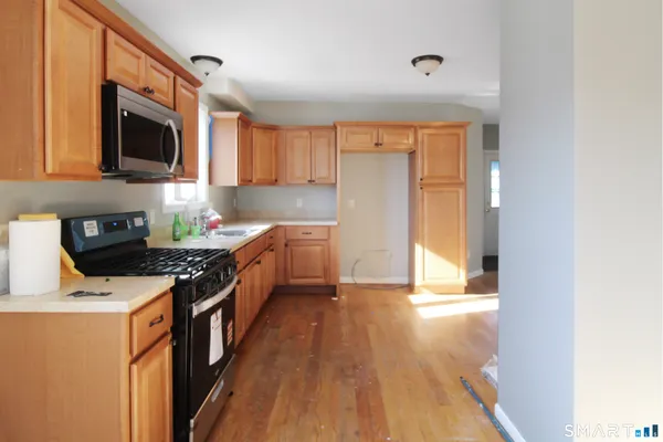 a kitchen with stainless steel appliances a stove top oven a sink a refrigerator white cabinets and wooden floor