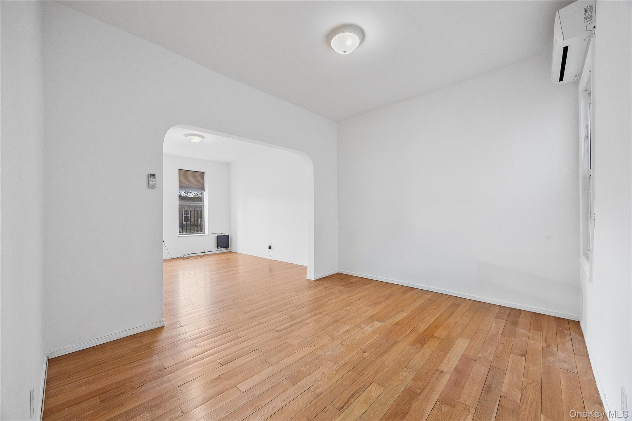 71-11 68th Street Queens, NY 11385 - Photo 3 of 24 Spare room featuring arched walkways, light wood-type flooring, and a wall unit AC