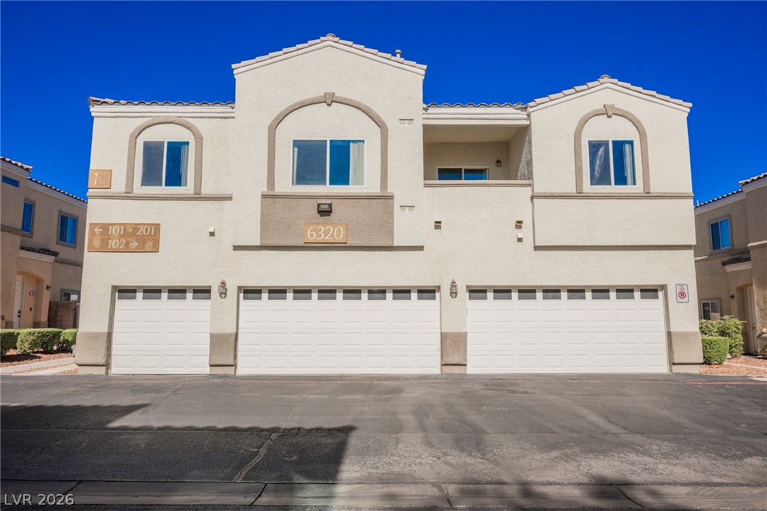 6320 Snap Ridge Street, Unit 201 North Las Vegas, NV 89081 - Photo 48 of 56 A cream-colored multi-level building presents a structured facade with multiple garage doors and arched windows.