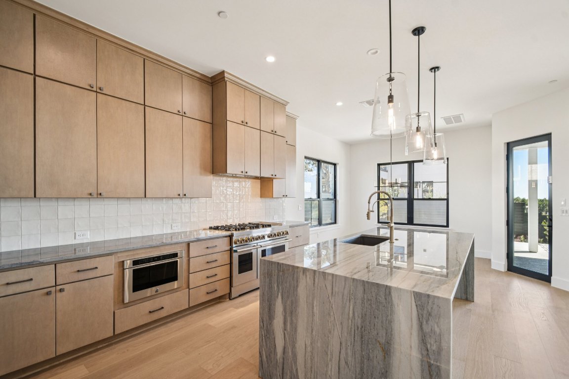 5903 Moondust Lane Austin, TX 78730 - Photo 12 of 37 a kitchen with stainless steel appliances kitchen island wooden floors and white cabinets