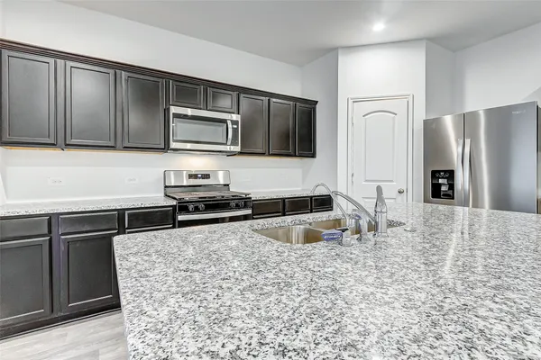 a kitchen with granite countertop a refrigerator and a stove top oven