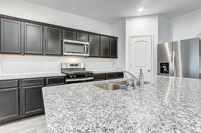 a kitchen with granite countertop a refrigerator and a stove top oven