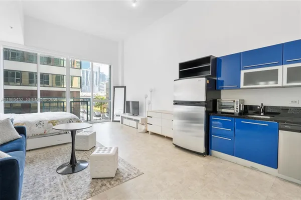 a living room with stainless steel appliances furniture a flat screen tv and a window