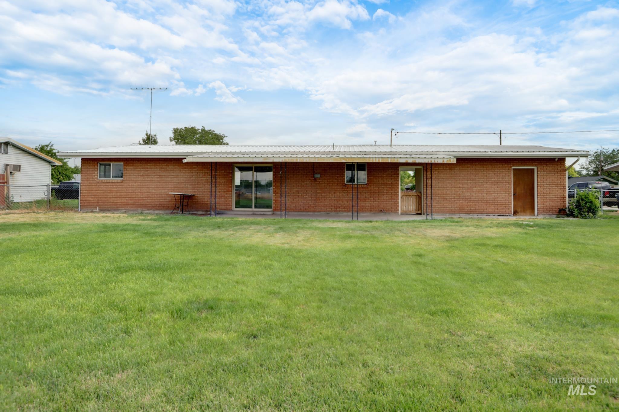 801 Thompson Avenue Nyssa, OR 97913 - Photo 42 of 46 Expansive green lawn with a brick exterior, white metal roof, sliding glass door, and multiple windows