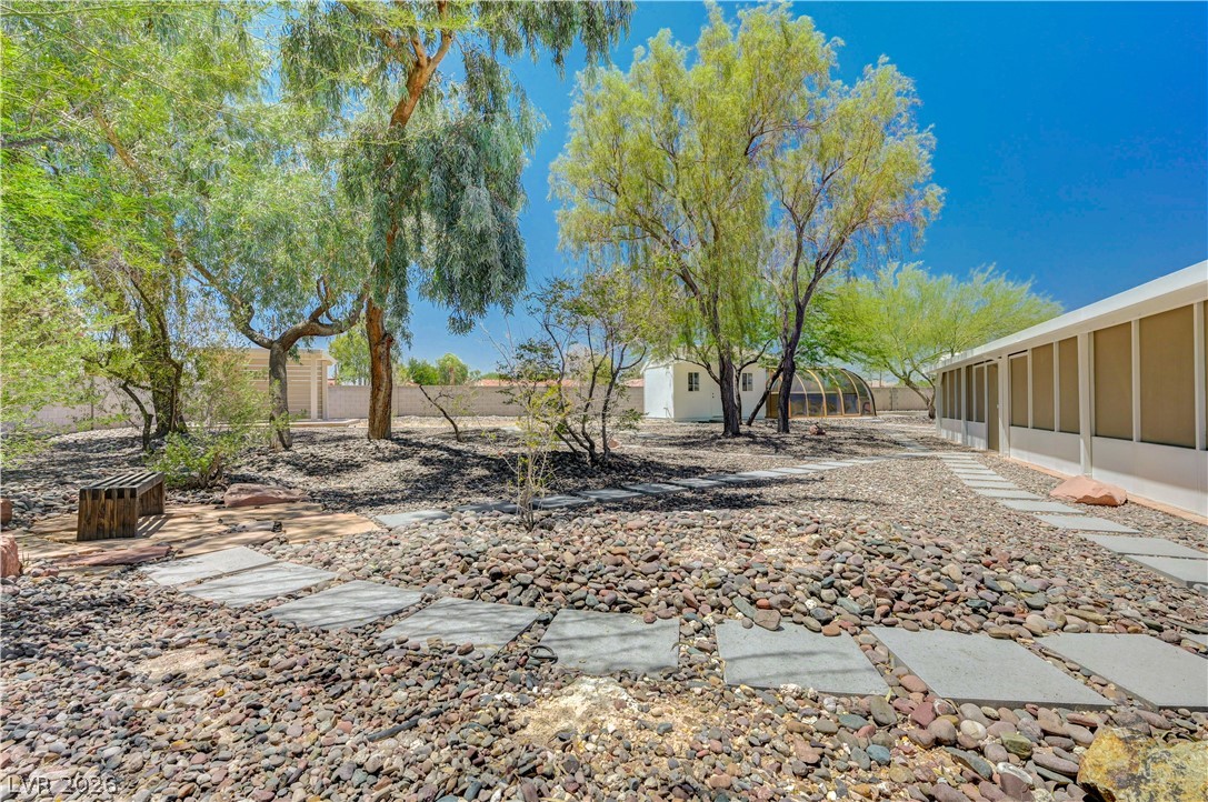 7631 Bermuda Road Las Vegas, NV 89123 - Photo 47 of 64 A tranquil desert landscape featuring established trees, pebble ground cover, and stepping stones leading to an outdoor greenhouse.