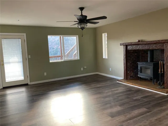 a view of an empty room with wooden floor fireplace and a window