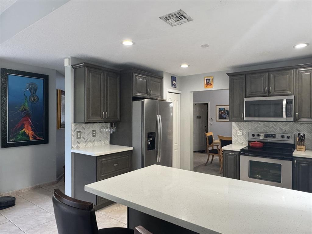 12353 Natalies Cove Road Cooper City, FL 33330 - Photo 9 of 24 a kitchen with stainless steel appliances kitchen island granite countertop a refrigerator a stove a sink a oven with a dining table and chairs