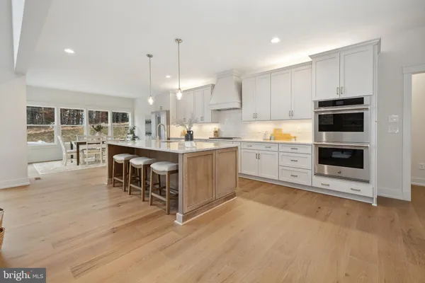 a kitchen with kitchen island granite countertop a stove a sink a oven a dining table and chairs with wooden floor