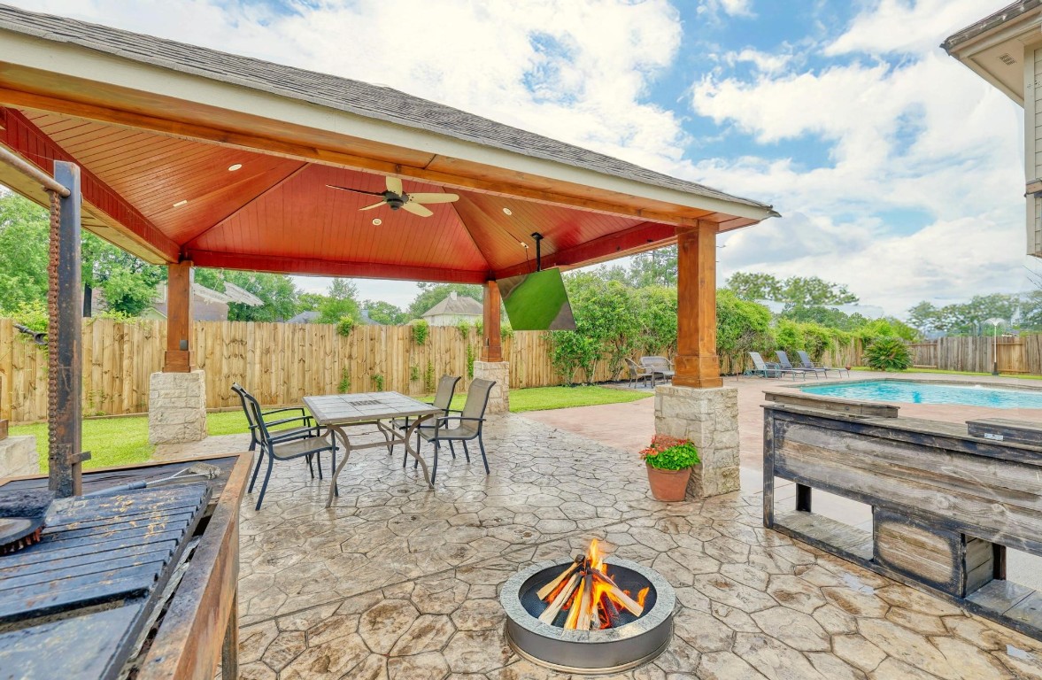 This impressive covered pavilion features a vaulted ceiling with fan, built-in TV mount, and plenty of space for outdoor dining. A cozy fire pit, grilling station, and stamped concrete patio create the perfect space for year-round entertaining.