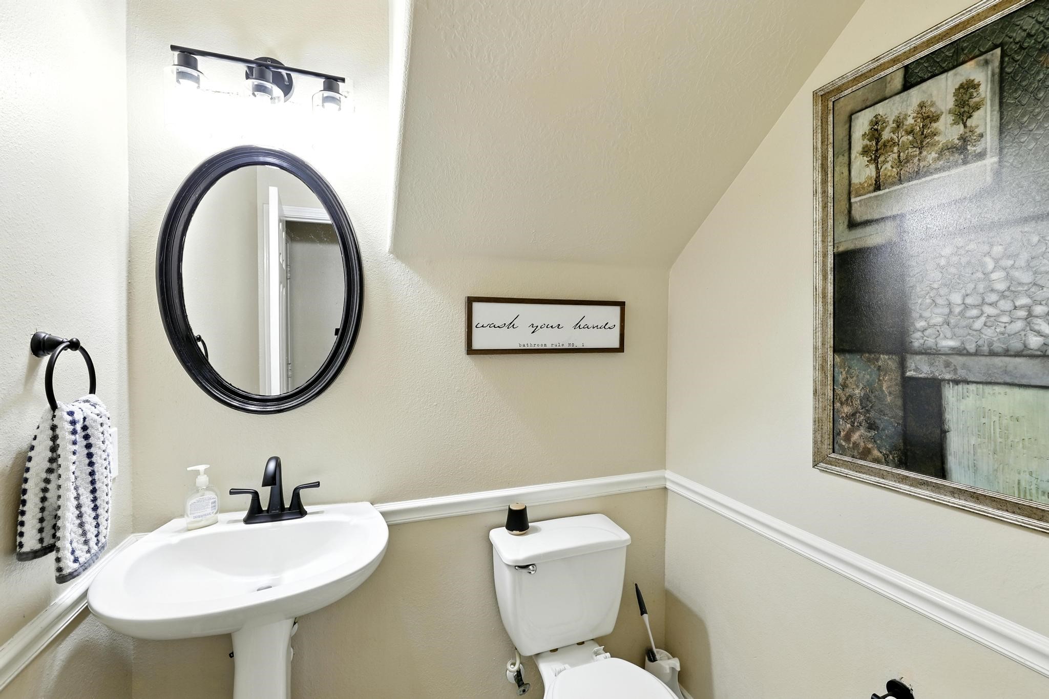 3002 Trinity Pass Court Spring, TX 77373 - Photo 12 of 22 Stylish half bath located just off the family room, featuring a pedestal sink, framed mirror, updated lighting, and decorative wall trim.