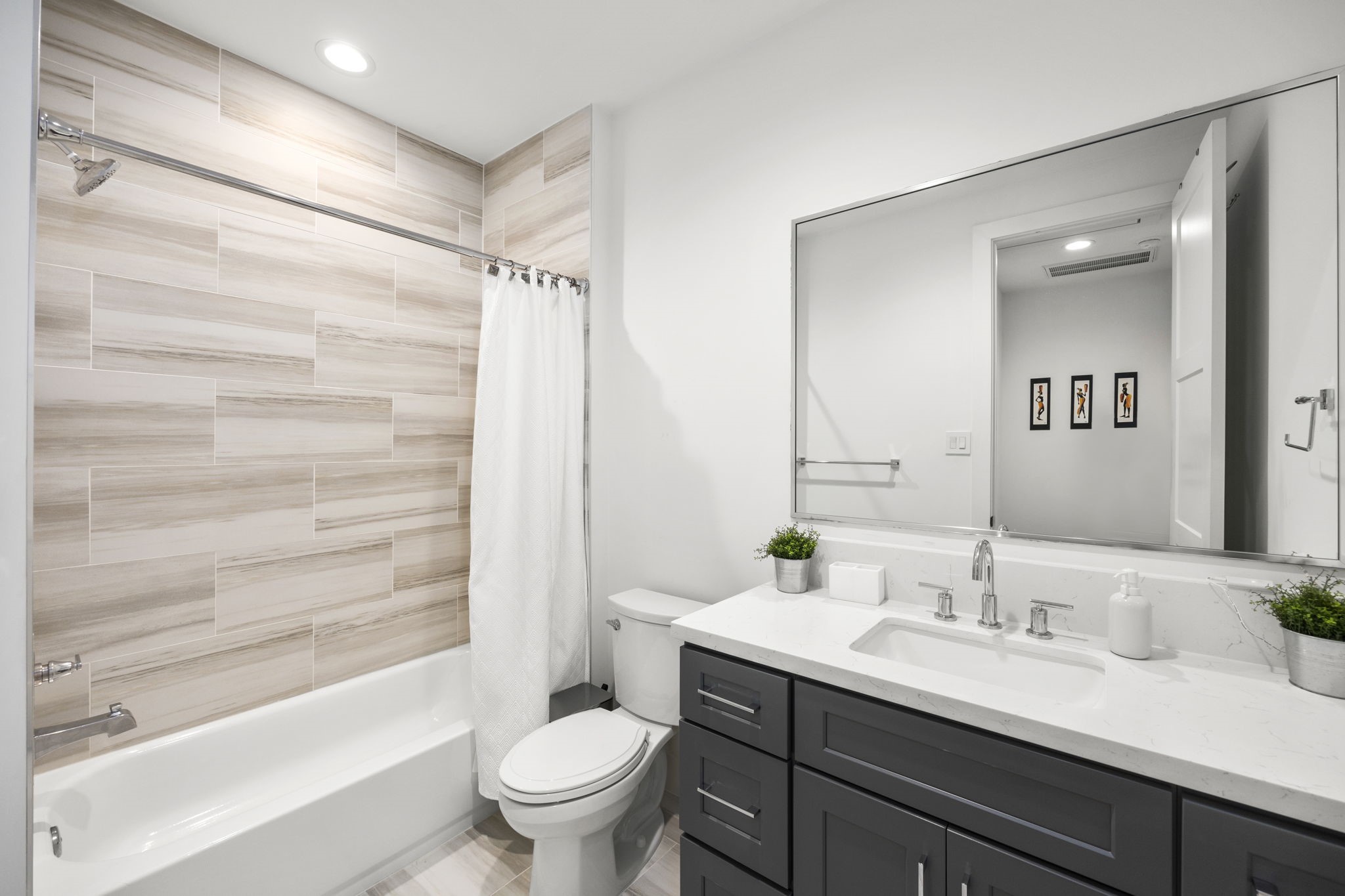 2411 Hazard Street Houston, TX 77019 - Photo 35 of 46 The secondary bathroom features modern, light wood-toned tile surrounding the bathtub and shower, complemented by a sleek vanity with polished chrome fixtures. The clean, bright aesthetic and practical layout make this bathroom an inviting and functional space.