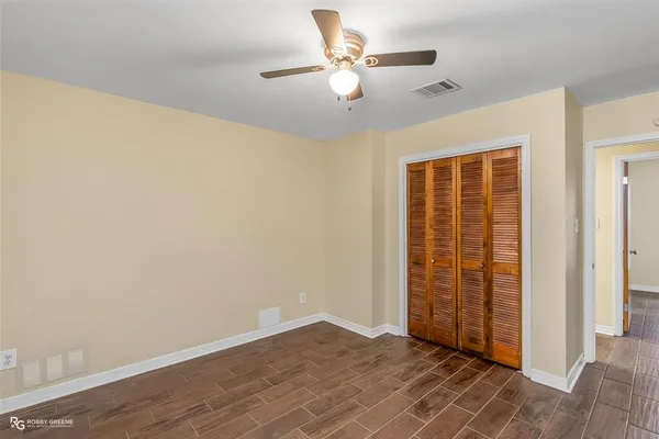 an empty room with wooden floor fan and windows