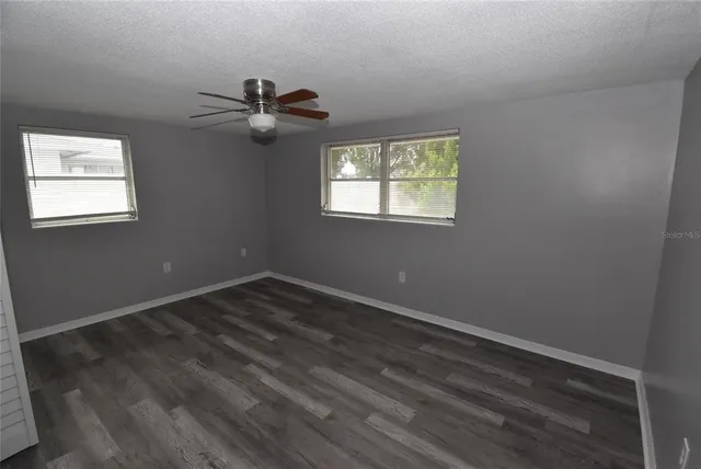 an empty room with wooden floor ceiling fan and windows
