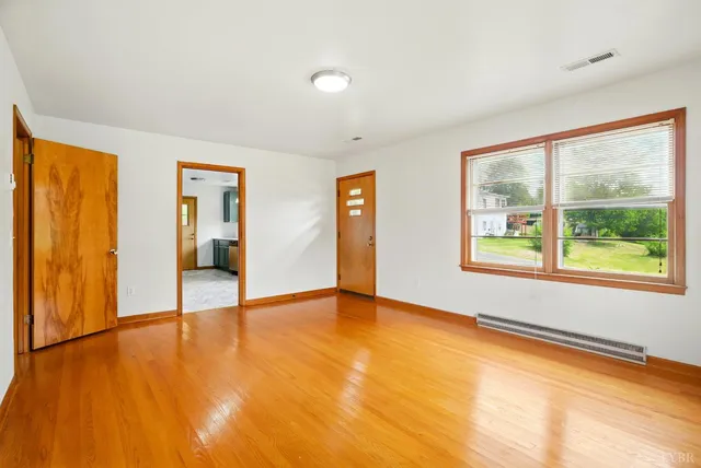 a view of an empty room with wooden floor and a window