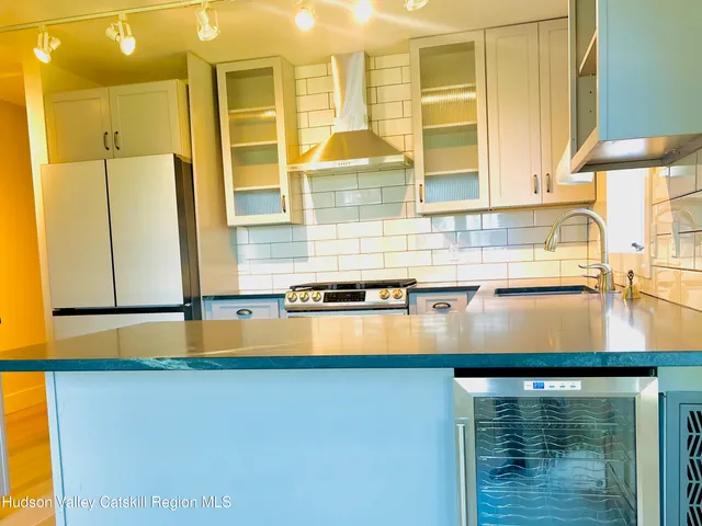 a kitchen with stainless steel appliances a refrigerator a sink a stove and white countertops with wooden floor