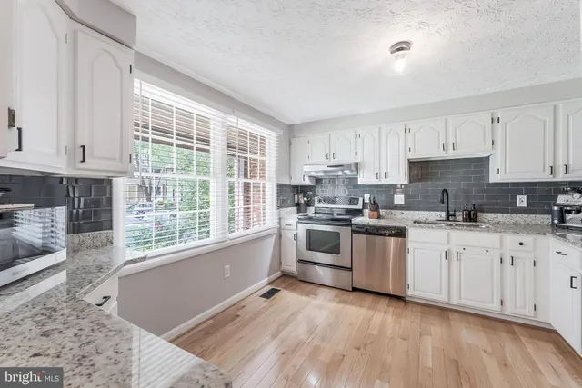 a kitchen with stainless steel appliances granite countertop a stove a sink and white cabinets
