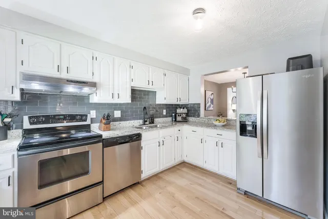 a kitchen with stainless steel appliances granite countertop white cabinets a sink a stove a refrigerator and white cabinets