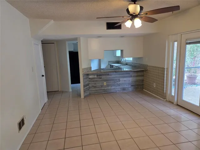 a room with a chandelier fan and kitchen view