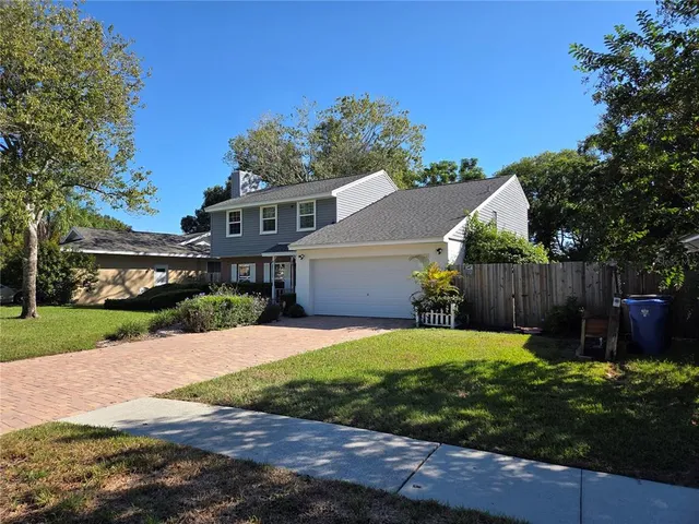 a house that is sitting in the grass with large trees and wooden fence