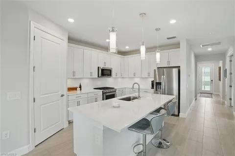 a kitchen with stainless steel appliances kitchen island granite countertop a refrigerator a sink dishwasher a stove and white cabinets with wooden floor