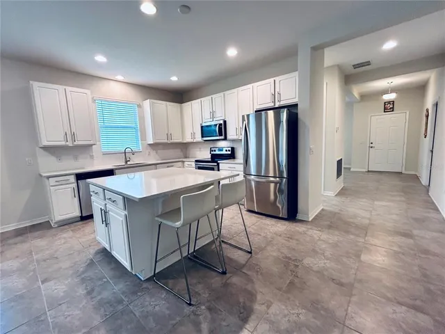 a kitchen with granite countertop a refrigerator a stove a sink dishwasher and white cabinets with wooden floor