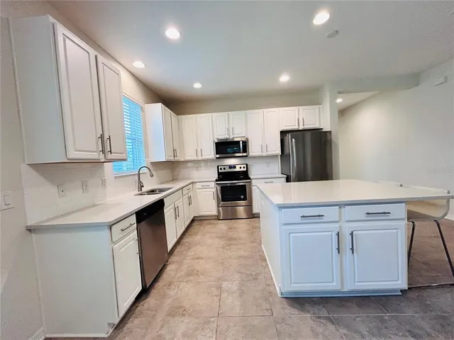 a kitchen with stainless steel appliances granite countertop a stove top oven a sink a refrigerator and white cabinets