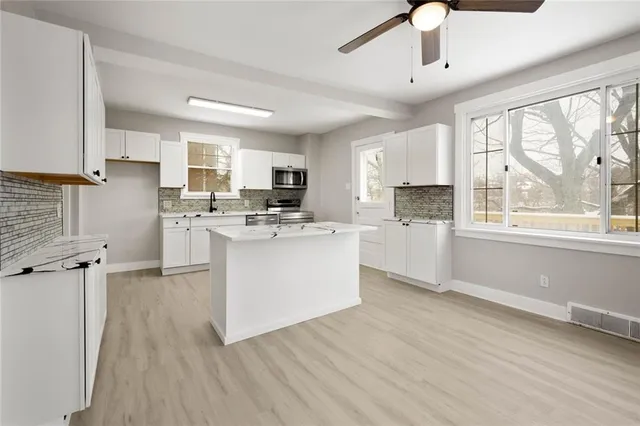 a kitchen with stainless steel appliances a stove top oven a sink a refrigerator white cabinets and wooden floor