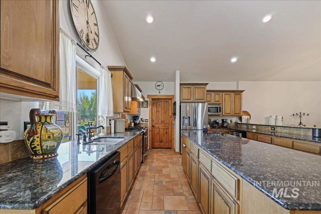7639 Elko Lane Middleton, ID 83644 - Photo 11 of 47 Kitchen featuring dark stone counters, brown cabinetry, appliances with stainless steel finishes, recessed lighting, and exhaust hood