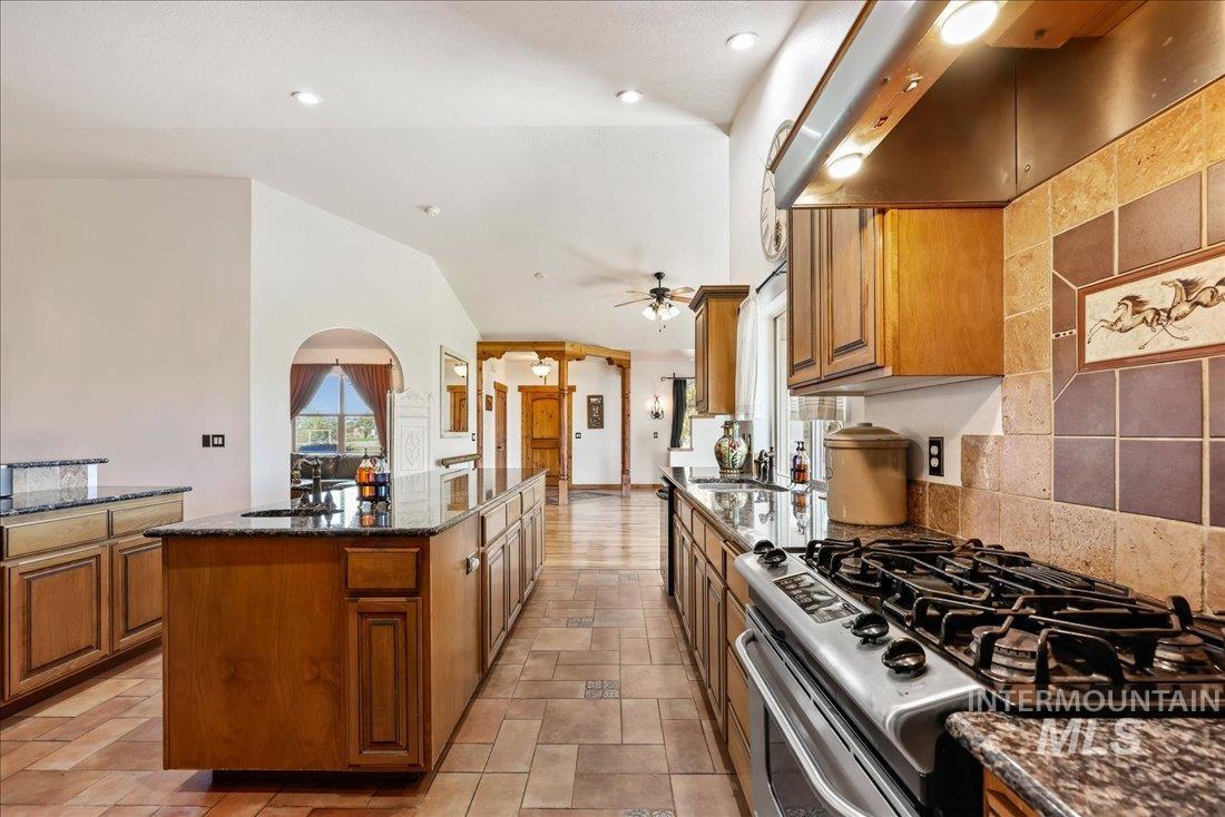 7639 Elko Lane Middleton, ID 83644 - Photo 15 of 47 Kitchen with dark stone counters, stainless steel range with gas stovetop, ventilation hood, brown cabinets, and stone tile flooring