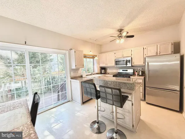 a kitchen with stainless steel appliances granite countertop a stove a refrigerator a kitchen island a table and chairs