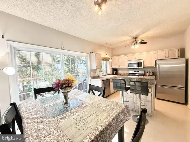 a kitchen with stainless steel appliances kitchen island granite countertop a refrigerator a stove a dining table and chairs with wooden floor