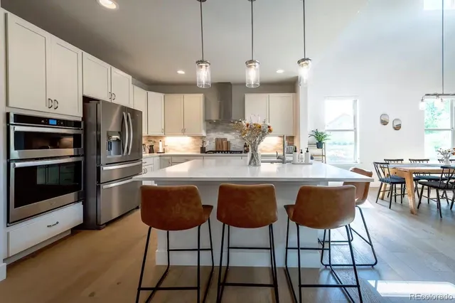 a kitchen with stainless steel appliances granite countertop a stove a sink a microwave a refrigerator a dining table and chairs with wooden floor