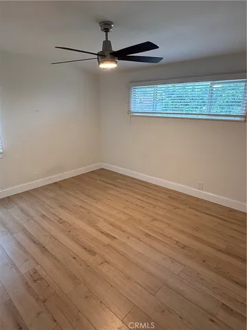 an empty room with wooden floor fan and windows