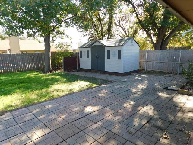 a view of a small yard in front of a house with large trees and wooden fence
