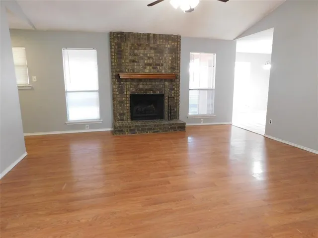 an empty room with wooden floor fireplace and windows