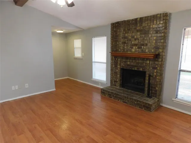 an empty room with wooden floor fireplace and windows