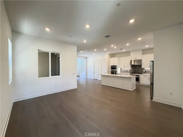 a large kitchen with kitchen island a sink a stove a refrigerator and white cabinets with wooden floor