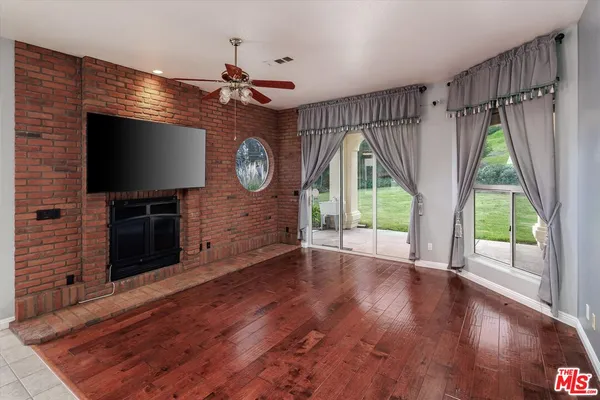 a view of a livingroom with wooden floor a ceiling fan and a fireplace