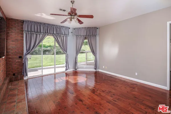 an empty room with wooden floor fan and a large window