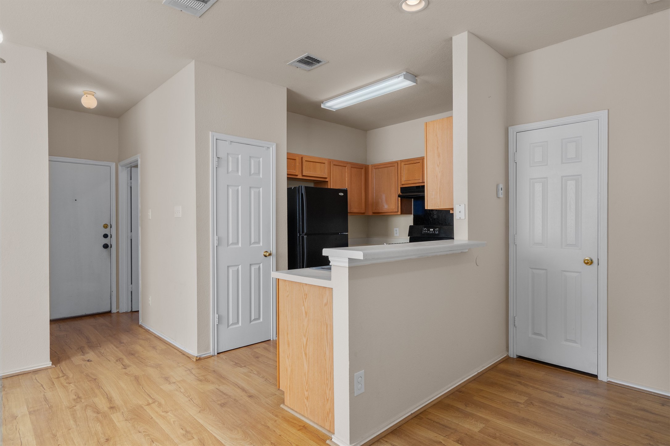 13720 Harris Ridge Boulevard, Unit A Pflugerville, TX 78660 - Photo 7 of 27 Kitchen with light countertops, a peninsula, black appliances, light wood-style flooring, and light wood finish cabinets