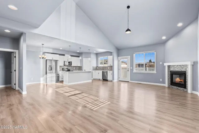 a view of an empty room with wooden floor and a kitchen