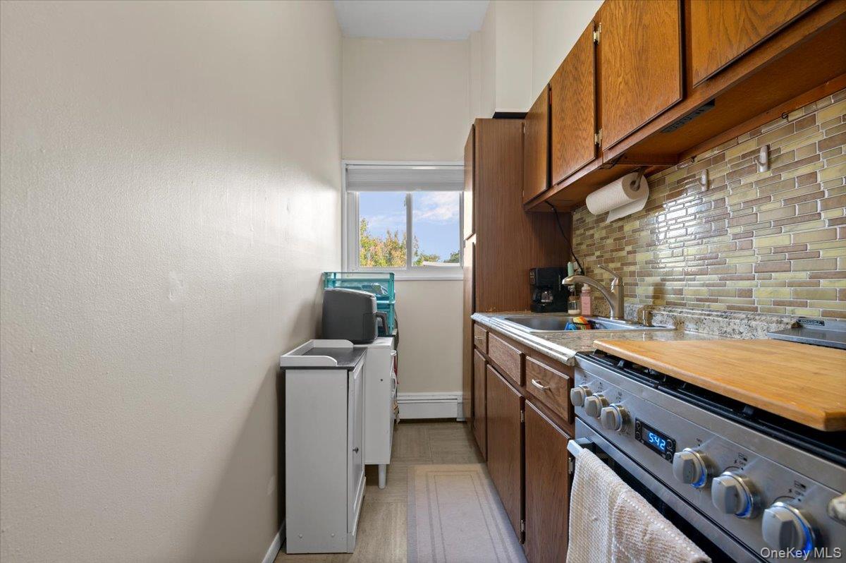 267 North Newbridge Road, Unit 2D Levittown, NY 11756 - Photo 17 of 22 Galley kitchen featuring wood-finish cabinetry, stainless steel range, and a tiled backsplash