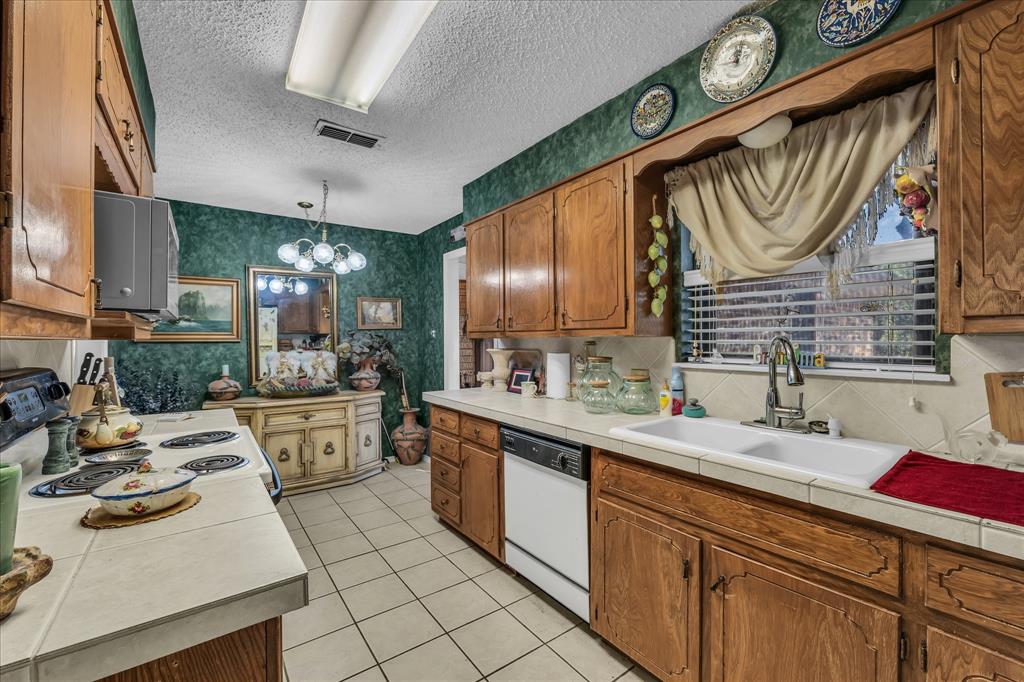 3405 Edna Avenue Waco, TX 76708 - Photo 13 of 29 Kitchen featuring wallpapered walls, brown cabinetry, tile countertops, pendant lighting, and white appliances