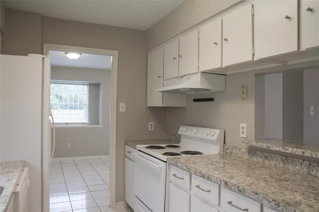 a kitchen with granite countertop a stove a sink and white cabinets