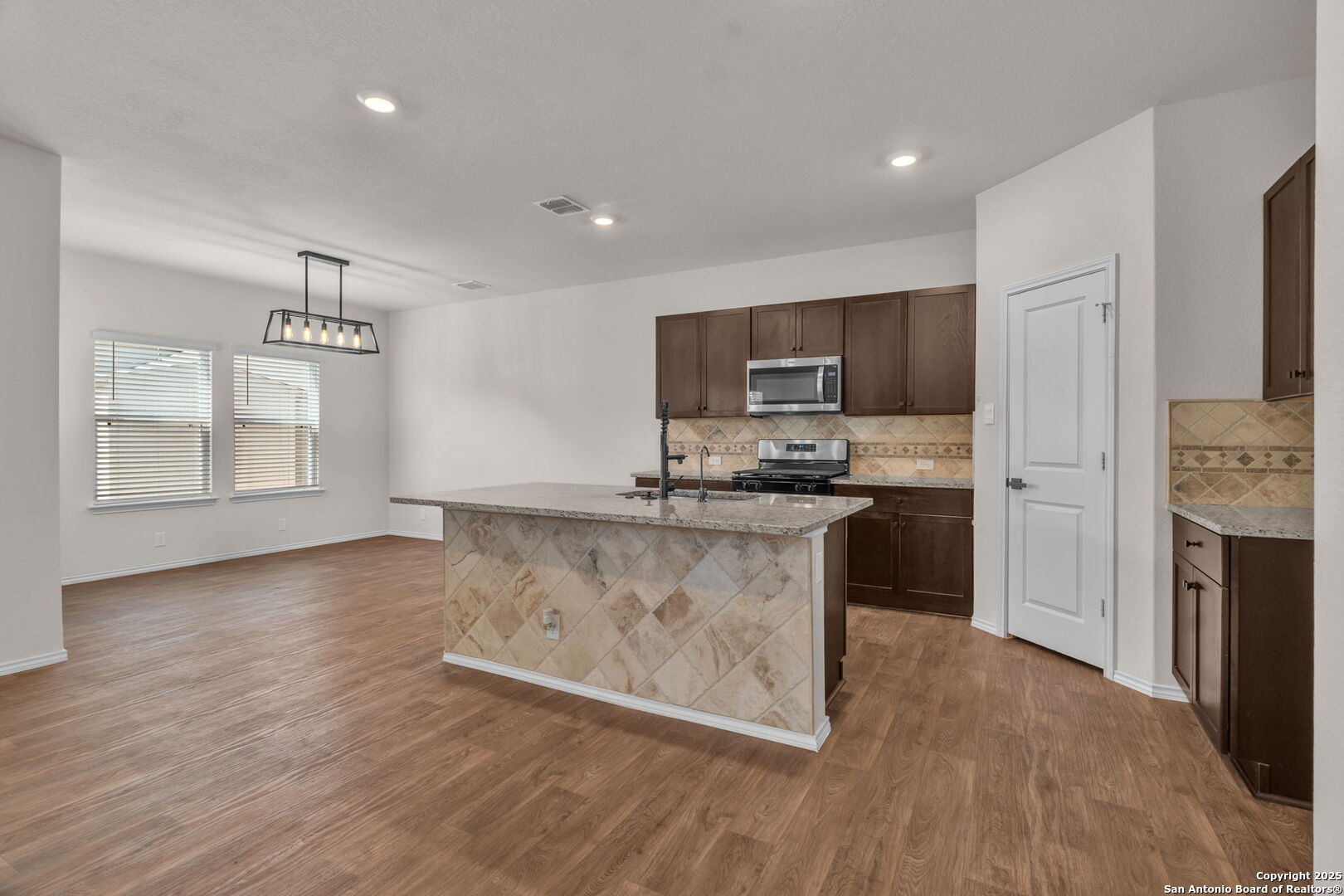 105 Honors Street Floresville, TX 78114 - Photo 8 of 36 a kitchen with granite countertop a stove top oven a sink dishwasher a refrigerator and a microwave oven with wooden floor