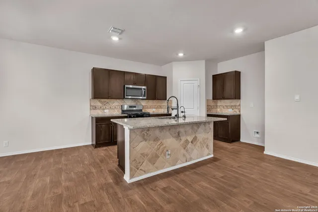 a kitchen with granite countertop a stove top oven a sink dishwasher a refrigerator and a microwave with wooden floor