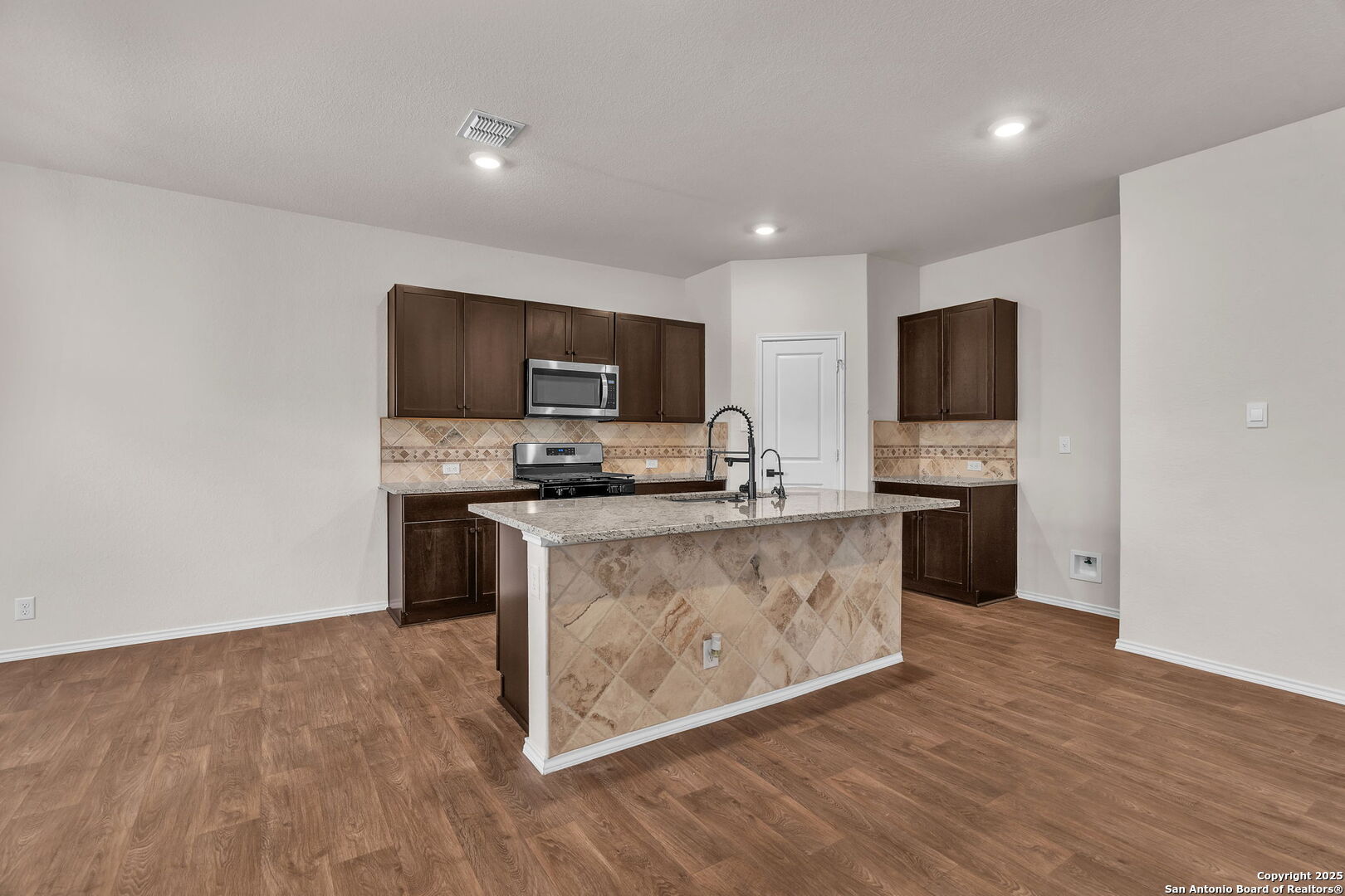 105 Honors Street Floresville, TX 78114 - Photo 10 of 36 a kitchen with granite countertop a stove top oven a sink dishwasher a refrigerator and a microwave with wooden floor