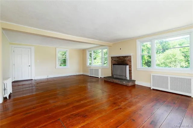 an empty room with wooden floor fireplace and windows