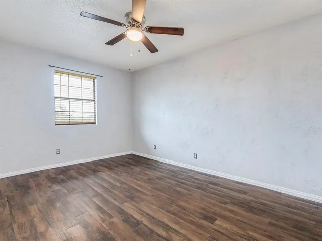an empty room with wooden floor fan and windows